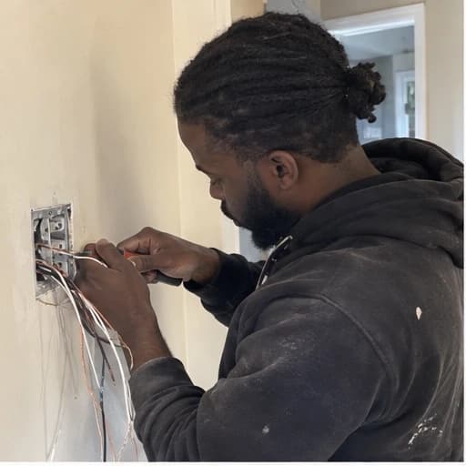 Electrician preparing wires at an open electrical wall box.